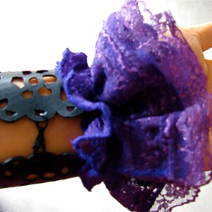 K&ouml;nnte beinhalten: Ein schwarzes Lederarmband mit einem zarten Spitzenmuster, verziert mit einer gro&szlig;en violetten und lavendelfarbenen Spitzenr&uuml;sche.