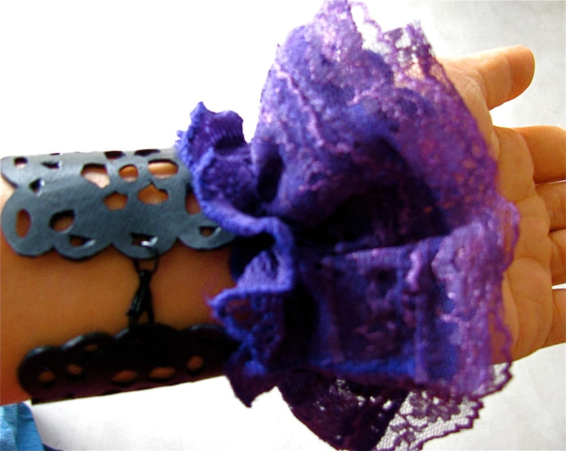 K&ouml;nnte beinhalten: Ein schwarzes Lederarmband mit einem zarten Spitzenmuster, verziert mit einer gro&szlig;en violetten und lavendelfarbenen Spitzenr&uuml;sche.