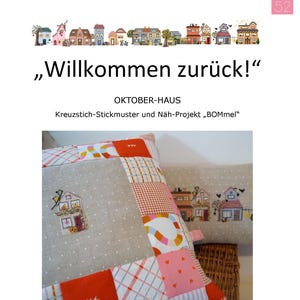 May include: Two decorative cushions with a patchwork design. One cushion features a stitched house, the other has a row of houses. The text "Willkommen zurück!" and "OKTOBER-HAUS" are visible.