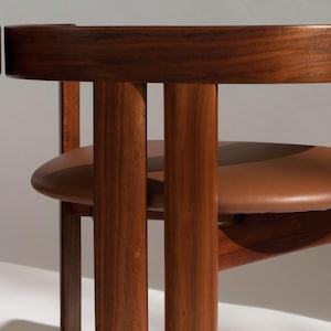 May include: Close-up of two wooden chairs with brown leather seats. The chairs have a curved backrest and vertical wooden supports. The wood has a rich, dark finish, and the seats are a warm brown color.