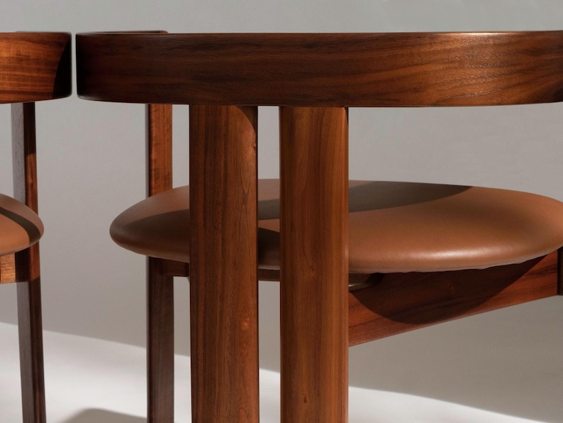 May include: Close-up of two wooden chairs with brown leather seats. The chairs have a curved backrest and vertical wooden supports. The wood has a rich, dark finish, and the seats are a warm brown color.