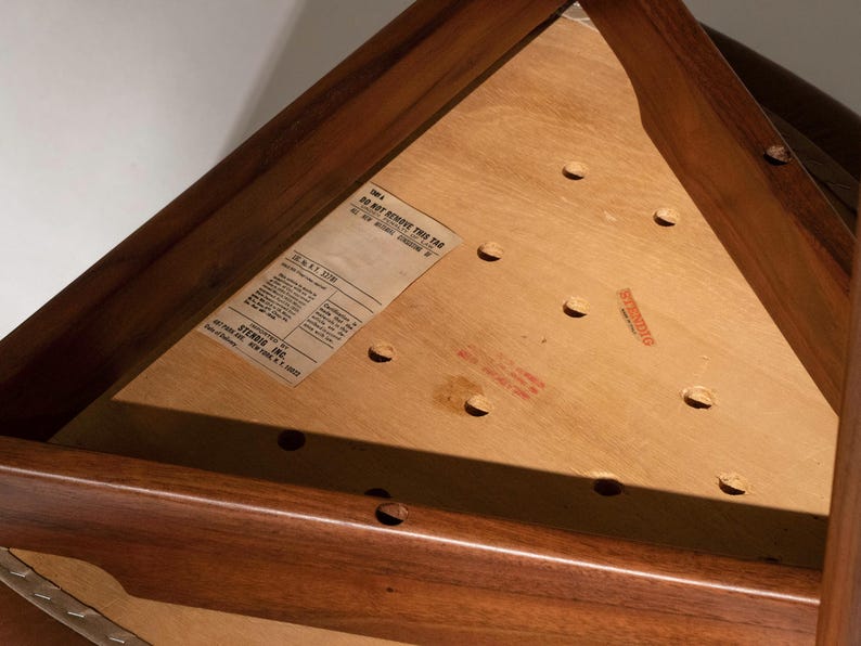 May include: Close-up of a wooden triangular table. The table has a dark brown frame and a light brown surface with several holes. A label is affixed to the surface with text that reads "DO NOT REMOVE THIS TAG".