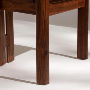 May include: Close-up of a wooden chair base. The chair legs are a rich, dark brown with visible wood grain. The design features a sturdy, minimalist aesthetic, showcasing the natural beauty of the wood.