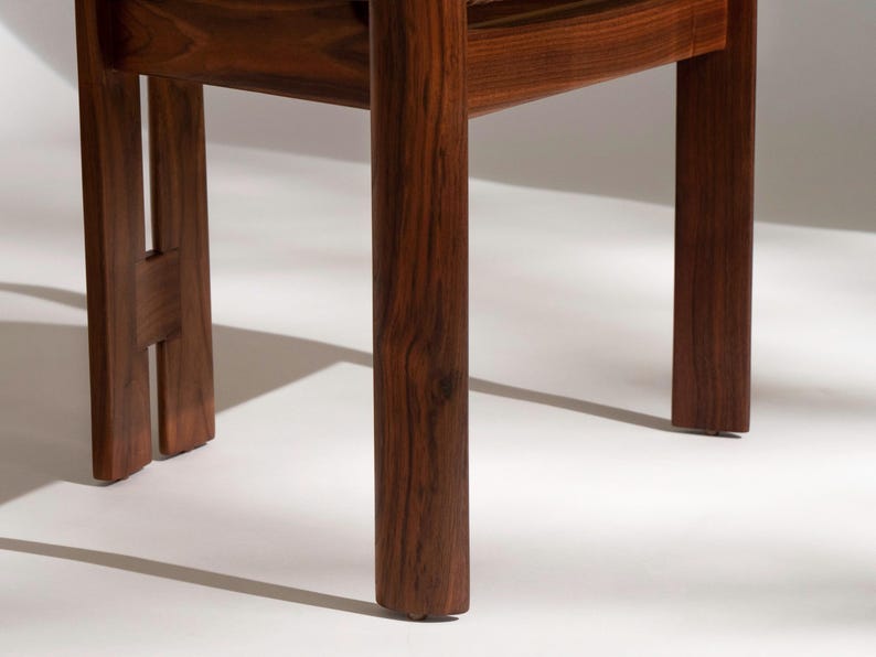 May include: Close-up of a wooden chair base. The chair legs are a rich, dark brown with visible wood grain. The design features a sturdy, minimalist aesthetic, showcasing the natural beauty of the wood.