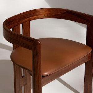 May include: A wooden chair with a curved back and a brown leather seat. The chair has a dark wood frame and a minimalist design. The seat is approximately 18 inches wide and 16 inches deep.