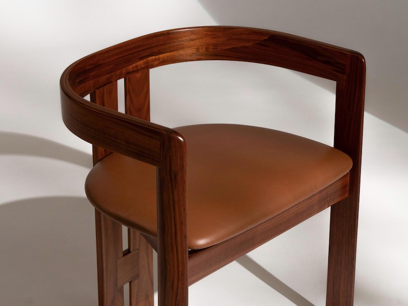 May include: A wooden chair with a curved back and a brown leather seat. The chair has a dark wood frame and a minimalist design. The seat is approximately 18 inches wide and 16 inches deep.