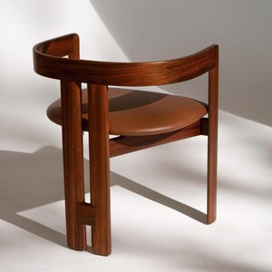 May include: A mid-century modern chair with a curved wooden back and frame. The seat is a round, brown leather cushion. The chair is made of dark wood and has a minimalist design, suitable for a living room or office.