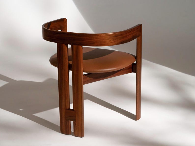 May include: A mid-century modern chair with a curved wooden back and frame. The seat is a round, brown leather cushion. The chair is made of dark wood and has a minimalist design, suitable for a living room or office.