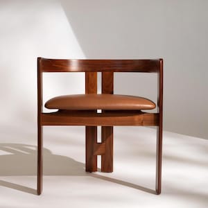 May include: A mid-century modern chair with a dark wood frame and a brown leather seat. The chair has a rectangular back and a unique design with a horizontal support. The chair is approximately 30 inches tall.