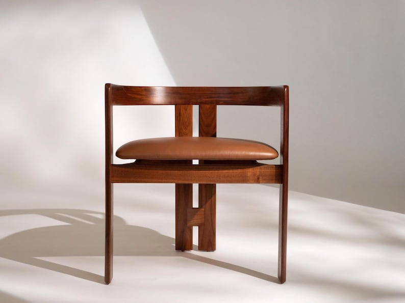 May include: A mid-century modern chair with a dark wood frame and a brown leather seat. The chair has a rectangular back and a unique design with a horizontal support. The chair is approximately 30 inches tall.