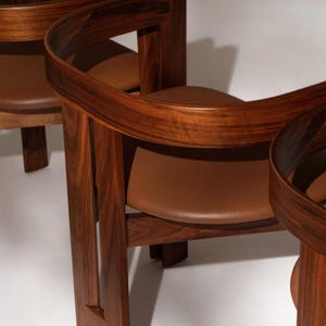 May include: Three wooden chairs with curved backs and brown leather seats. The chairs are made of dark wood and have a modern design. The seats are a light brown color.