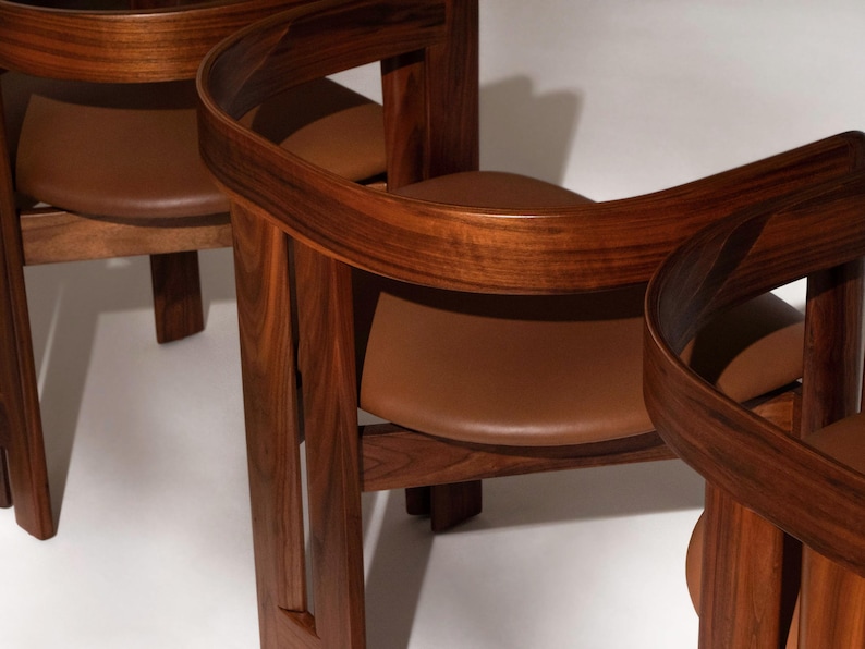 May include: Three wooden chairs with curved backs and brown leather seats. The chairs are made of dark wood and have a modern design. The seats are a light brown color.