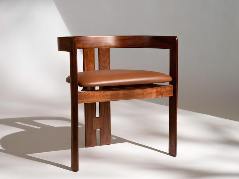 May include: A wooden chair with a brown leather seat. The chair has a minimalist design with a rectangular back and a seat that appears to float. The wood has a rich, dark finish. The chair's dimensions are approximately 30 inches high, 20 inches wide, and 20 inches deep.