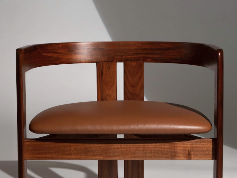 May include: A mid-century modern chair with a curved, dark wood frame and a brown leather seat. The chair has a minimalist design, showcasing the natural wood grain and the smooth texture of the leather. The backrest is curved for comfort.