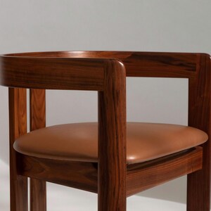 May include: A wooden chair with a curved back and armrests. The chair has a brown leather seat. The wood has a rich, dark finish. The chair is a mid-century modern design.