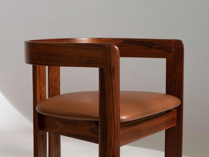 May include: A wooden chair with a curved back and armrests. The chair has a brown leather seat. The wood has a rich, dark finish. The chair is a mid-century modern design.
