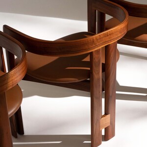 May include: Three wooden chairs with curved backs and brown leather seats. The chairs have a warm, natural wood finish and a minimalist design. The chairs are set against a white background.