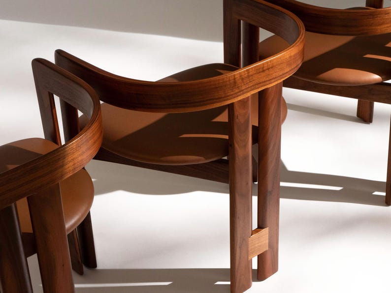 May include: Three wooden chairs with curved backs and brown leather seats. The chairs have a warm, natural wood finish and a minimalist design. The chairs are set against a white background.