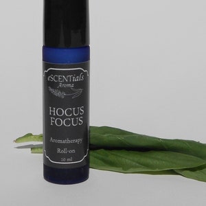 May include: A blue glass roll-on bottle with a black label that says "escenTials Aroma HOCUS FOCUS Aromatherapy Roll-on 10 ml"