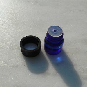 May include: A small blue glass bottle with a black cap. The bottle is filled with a clear liquid.