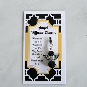 May include: A silver angel diffuser charm with black lava beads. The charm has a heart-shaped pendant and wings. The card reads "Angel Diffuser Charm" and "Wherever You Go Whatever You Do May Your Guardian Angel Watch Over You".