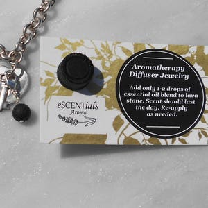 May include: A silver-toned aromatherapy diffuser jewelry necklace with a heart and key charm, a black lava stone, and a black cap. A card with text reads "Aromatherapy Diffuser Jewelry".