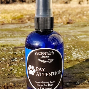May include: A blue glass bottle with a black spray nozzle and a white label that reads "eSCENTials Aroma PAY ATTENTION Aromatherapy Focus Spray For Dogs 4 fl. oz. (120 ml)"