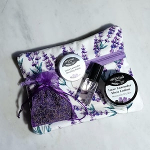 May include: A lavender-themed gift set featuring a zippered pouch with a lavender floral print, a small bag of dried lavender, a small roller bottle, and two tins labeled "Luxe Lavender". The set is designed for skincare and relaxation.