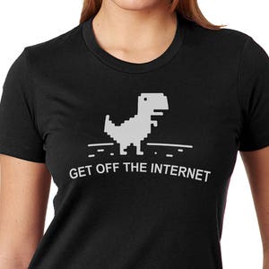 Puede incluir: Camiseta negra con un gr&aacute;fico de dinosaurio pixelado blanco y el texto "Get Off The Internet".