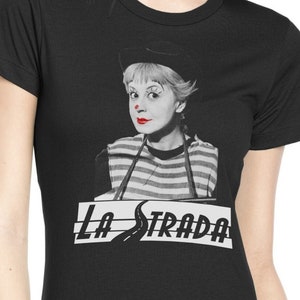 May include: Black t-shirt with a black and white image of a woman dressed as a clown. The text "LA STRADA" is printed in white below the image.