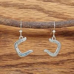 May include: A pair of silver horseshoe earrings with a hammered texture. The earrings are dangle style with a small bead at the top.