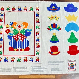 May include: A white fabric panel with a large clown illustration in red, white, blue, and orange. The panel also features various hat designs and small clown figures around the border, ideal for a sewing project.