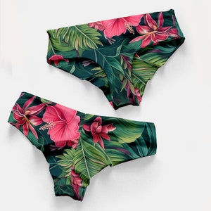 May include: Two bikini bottoms featuring a vibrant tropical print with large pink hibiscus flowers and lush green palm leaves set against a dark background. The swimwear pieces have a high-cut leg design and a wide waistband for a secure fit.