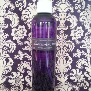 May include: A purple glass spray bottle with a white top, filled with a lavender-colored liquid. The label reads "Lavender Mist" and "Shake and Spritz". The background is a purple and white floral pattern.