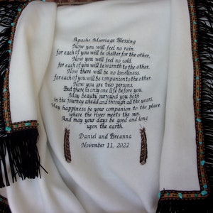 May include: White blanket with black fringe and turquoise beads. The blanket has an embroidered Apache Marriage Blessing with the text "Now you will feel no rain. for each of you will be shelter for the other. Now you will feel no cold. for each of you will be warmth to the other. Now there will be no loneliness. for each of you will be companion to the other. Now you are two persons. But there is only one life before you May beauty surround you both in the journey ahead and through all the years May happiness be your companion to the place where the river meets the sun. And may your days be good and long upon the earth. Daniel and Breanna November 11, 2022"