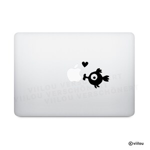 Könnte beinhalten: Ein weißer Laptop mit einem schwarzen Aufkleber, der einen Cartoon-Vogel zeigt, der das Apple-Logo küsst, mit einem Herz darüber. Der Vogel hat ein großes Auge und kleine Flügel. Der Aufkleber befindet sich auf der Oberseite des Laptops.