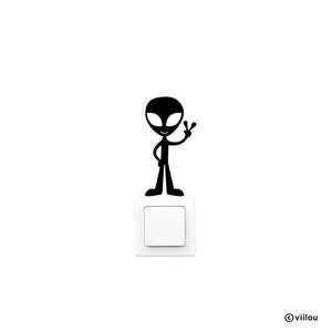 Pode incluir: Adesivo preto e branco de um alienígena com um sinal de paz em um interruptor de luz branco.