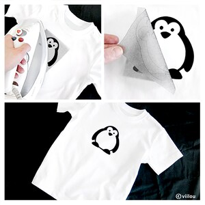 May include: A white t-shirt with a black penguin design ironed on. The penguin is facing forward with its wings outstretched and has a small beak and eyes.