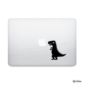 Könnte beinhalten: Schwarzer Dinosaurier-Aufkleber auf einem weißen Laptop. Der Dinosaurier ist eine Cartoon-Illustration mit einem lächelnden Gesicht und einem stacheligen Rücken. Der Laptop hat ein Apple-Logo. Der Aufkleber befindet sich auf der rechten Seite.