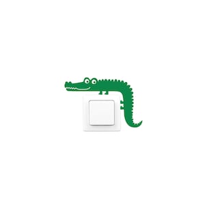 Op de afbeelding: Een groene alligator sticker op een witte lichtschakelaar.