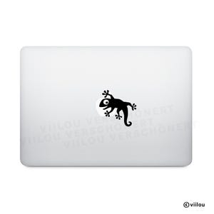 Könnte beinhalten: Ein schwarzer Eidechsenaufkleber auf einem weißen Laptop. Die Eidechse befindet sich auf einem weißen, kreisförmigen Hintergrund. Der Aufkleber ist eine Cartoon-Illustration mit einem großen Auge und einem eingerollten Schwanz.
