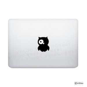 Può includere: Un laptop bianco con un adesivo a forma di gufo nero al centro. Il gufo è una semplice silhouette con un grande occhio rotondo. L'angolo in basso a destra del laptop ha il simbolo del copyright e la parola "viilou".