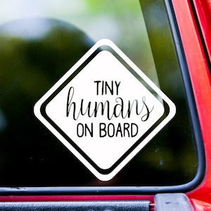 May include: White vinyl car sticker with a black diamond shape and the text "TINY humans ON BOARD".