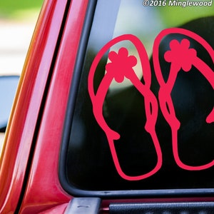 May include: A pair of pink flip-flop sandals with a flower design on the strap. The sandals are on a black background.