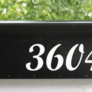 May include: Black mailbox with a red flag and white cursive numbers 3604.