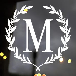 May include: White vinyl decal of a wreath with leaves and berries surrounding the letter "M".