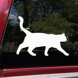 May include: White silhouette of a cat walking, applied to a car window.
