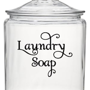 May include: A clear glass jar with a lid, labeled "Laundry Soap" in a decorative script font. The jar is empty and ready to be filled with laundry detergent.