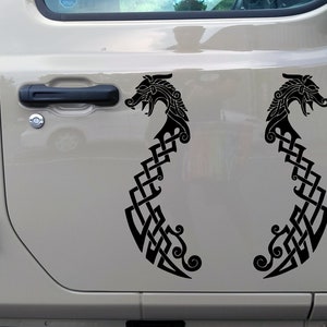 May include: A pair of black vinyl decals featuring a Celtic knot design with a dragon head at the top. The decals are applied to the doors of a light beige Jeep.