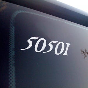 May include: White vinyl decal with the number sequence "50501" in a stylized font, affixed to a dark surface, likely a vehicle window. The numbers are clearly visible against the dark background.